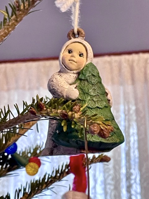 Tree ornament, child wearing snowsuit hugging small tree
