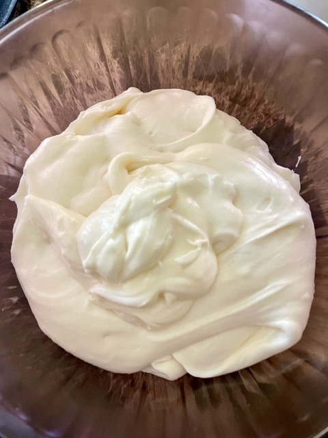 White cream cheese frosting in a reddish glass mixing bowl
