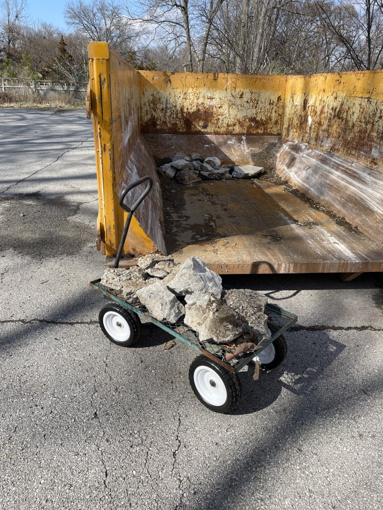 Large yellow roll-off construction dumpster with a flat cart holding chunks of concrete.